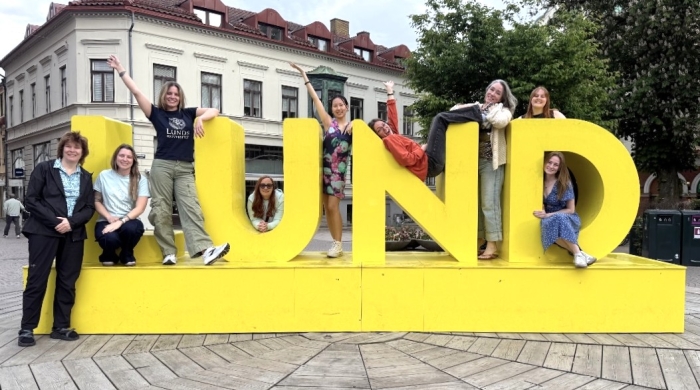 Students pose on and around a bright yellow sign reading "Lund"