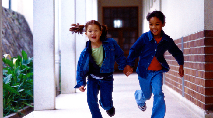 Two young girls run in a school corridor