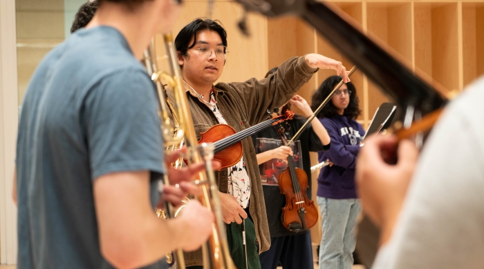 Sam Wu speaking to a rehearsal room of musicians, holding instruments