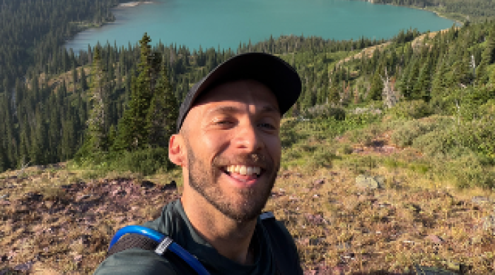 Photo of Joey Haavik hiking, body of water and mountains behind him