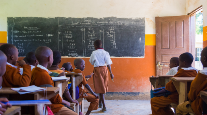 Children in uniforms in elementary school classroom sitting behind desks listening to teacher