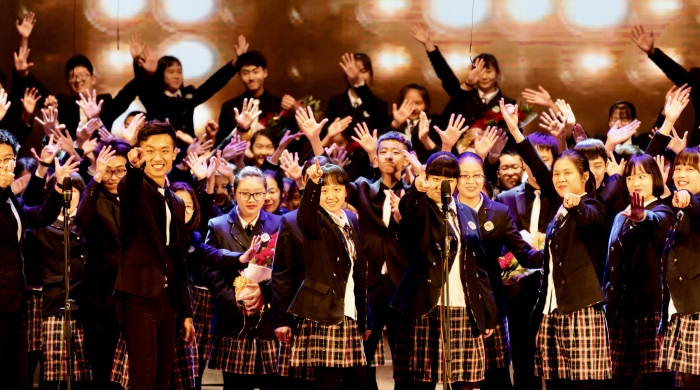 Chinese choir students in school uniforms cheering in front of spotlights