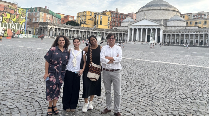Four researchers and scholars pose for a photo in a stone-paved plaza in Italy. 