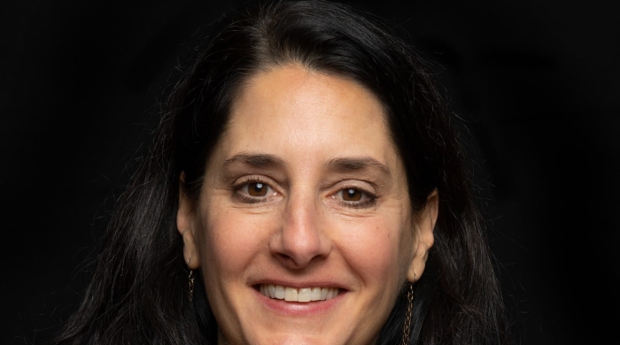 Headshot of Mary Helen Immordino-Yang smiling, wearing a black collared top, long earrings, and a necklace against a black background.