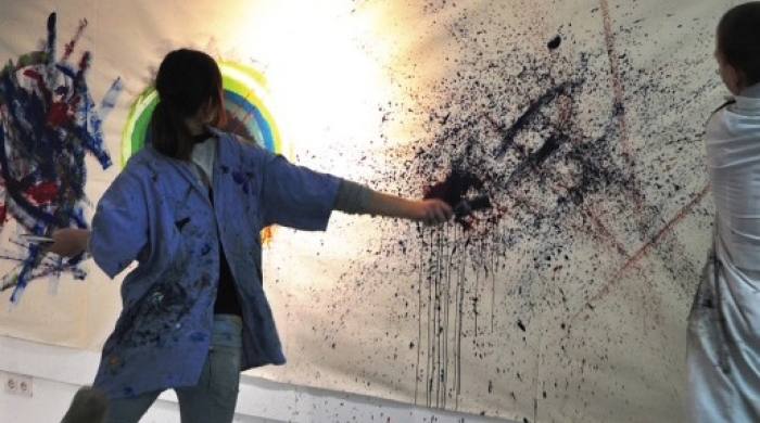 A child stands in front of a canvas, splatter painting