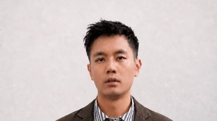 A young East Asian man with short black hair looks into the camera