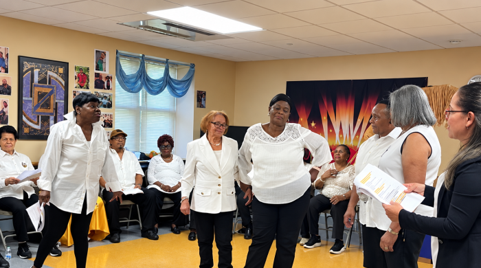 Six Breaking Ground resident drama therapy participants stand and rehearse while a circle of others sit and watch