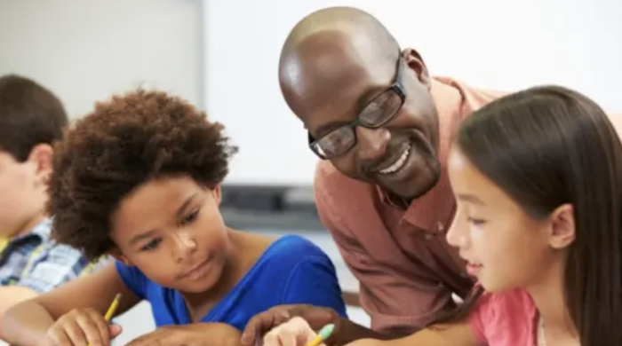 A Black teacher helping two students in classroom