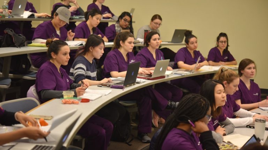 Students sitting in a lecture hall in scrubs.