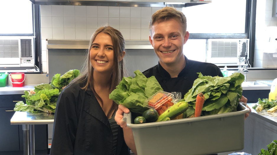Two students holding a bucket of vegetables.