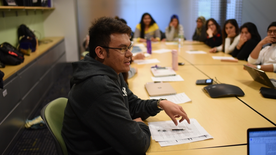 A student sitting at a conference table with his peers in the background.