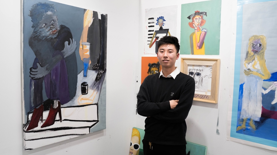Student in his studio with paintings on wall. 