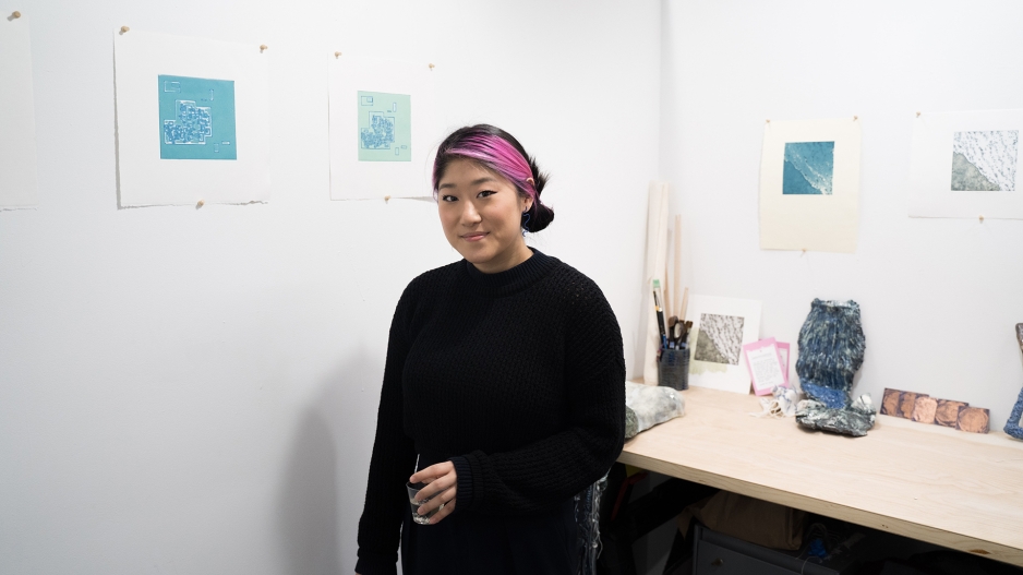 Student in studio with works on paper on wall. 