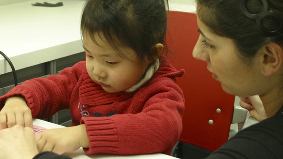 A speech-language pathologist working on an activity with a small child in red.