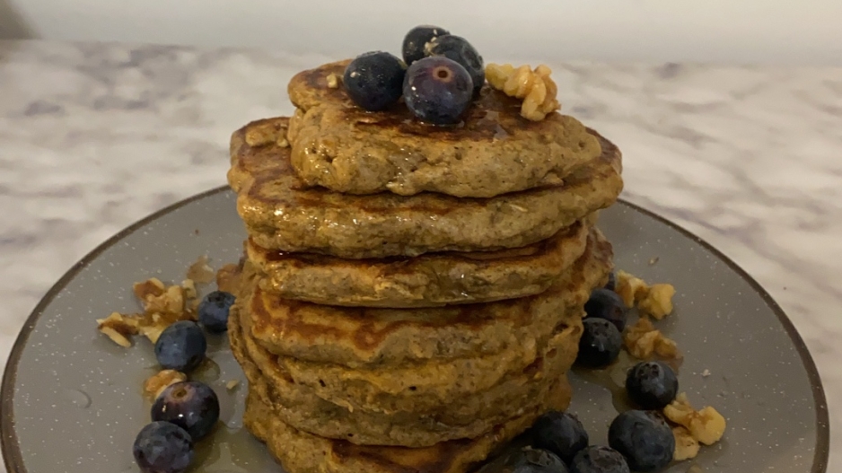A stack of pancakes on a plate topped with blueberries and walnuts.