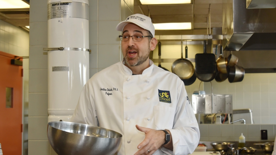 Jonathan Deutsch in a chef's white jacket holding a metal mixing bowl in a kitchen.