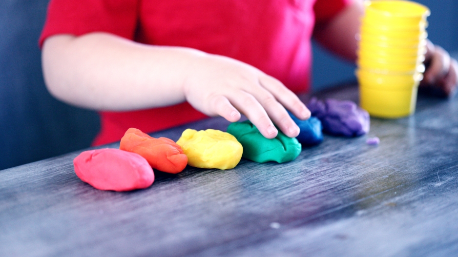A picture of the arms of a child playing with six colors of Play Dough