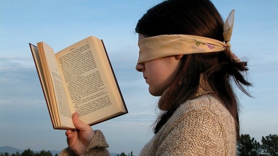 A girl holds a book in hand as though reading with handkerchief covering her eyes