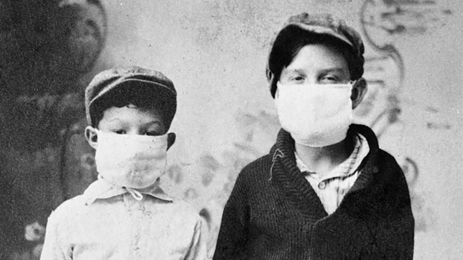 A black and white image of two young boys posing for a picture wearing masks during the Spanish flu