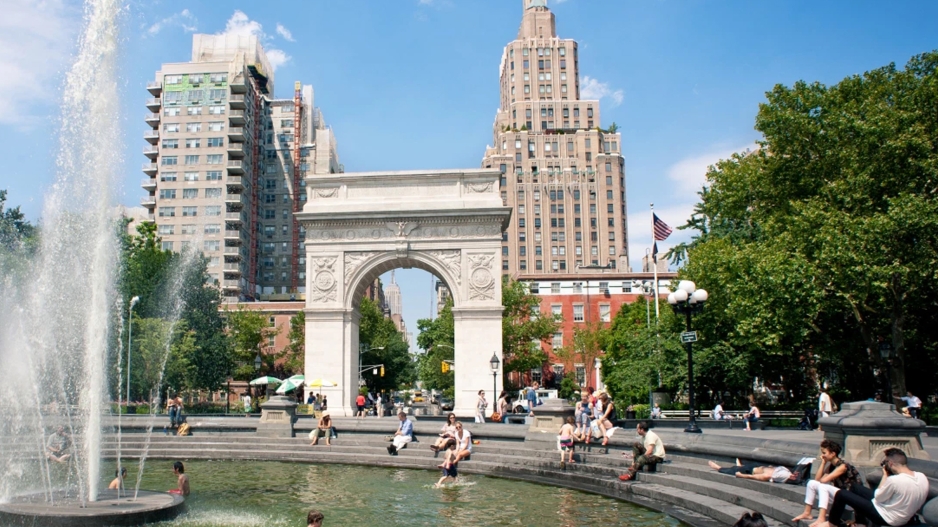 A photograph of the arch at Washington Square Park with a fountain in the foreground and people relaxing next to it
