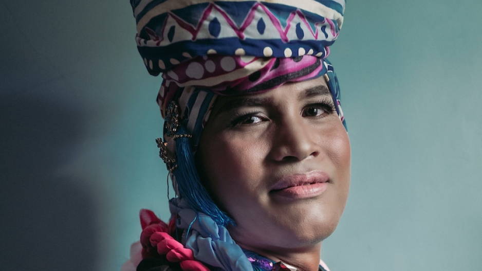 Indigenous gender expansive woman wearing traditional cultural clothing and smiling into the camera