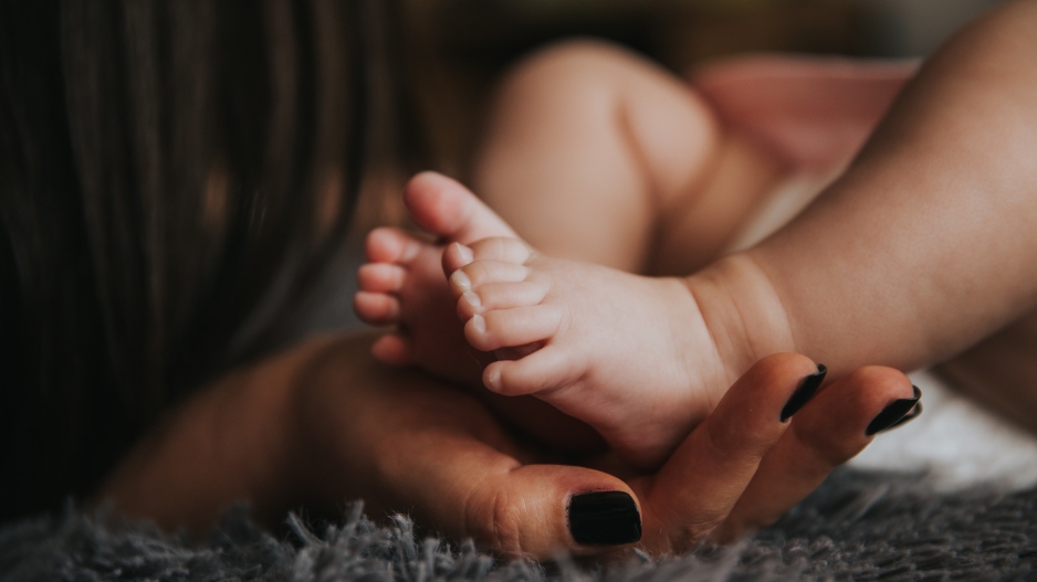A photo of an adult hand with painted fingernails holding the feet of an infant