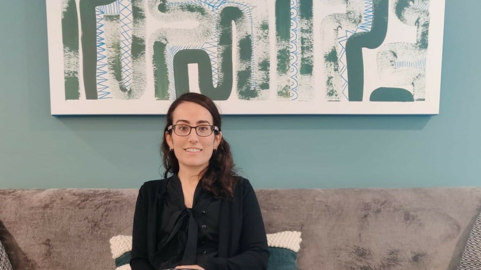 Meirav Rosenfeld sitting on a couch in front of an abstract piece of wall decor.