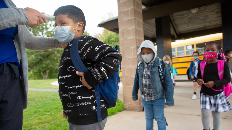 Young boy with mask gets temperature taken outside of school building