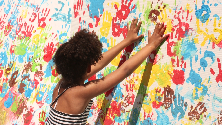 A woman pressing her hands to a large canvas filled with handprints in many different colors