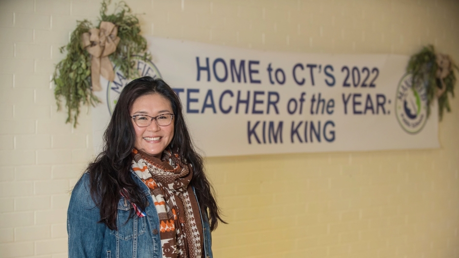 Kim King standing in front of banner that reads "Home to CT's 2022 Teacher of the Year: Kim King."
