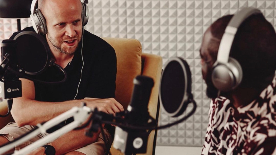 photo of two men with headphones on talking in a studio