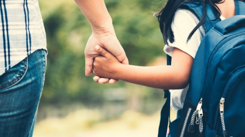 A child with a backpack holds a parent's hand.
