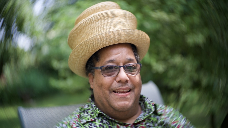 A photo portrait of Scott Alves Barton with a straw hat and a green flowered shirt.