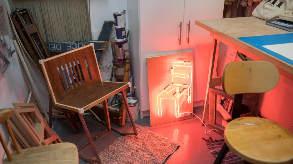 A BFA student's studio. A wooden chair appears next to a neon sign shaped like a chair. 