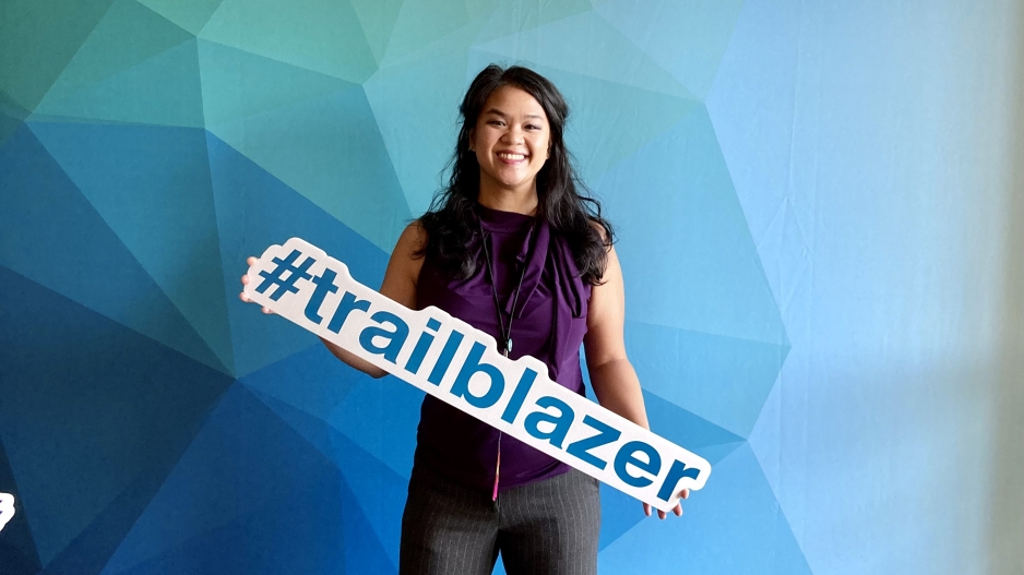 Annalissa Vicencio stands in front of a blue background holding a sign that says #trailblazer
