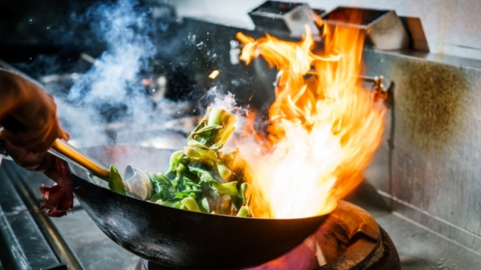 A photo of a wok with high flames and full of green vegetables.