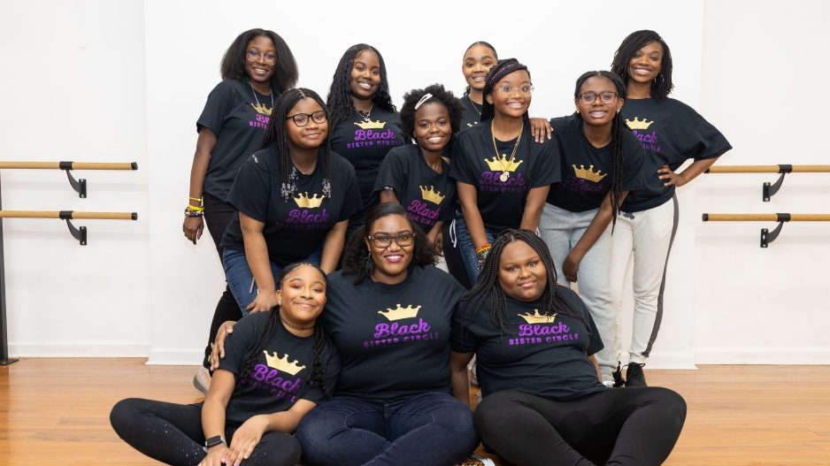 A group of Black women in matching t-shirts smile at the camera. 