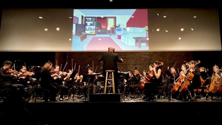 screen with cartoon playing and orchestra in front of it performing