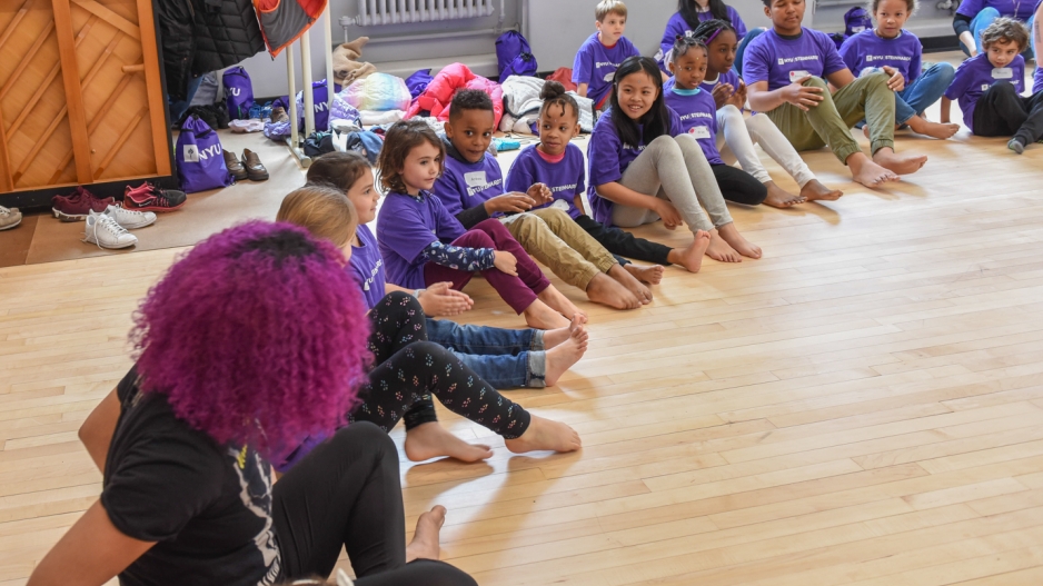 Dance instructor Katherine Jimenez, a woman with curly magenta hair, sits in a circle with children at Take Your Children to Work Day.