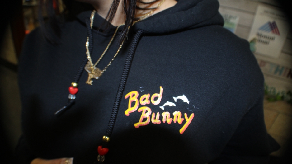 flash photograph of a someone wearing a black Bad Bunny sweatshirt and a gold necklace with their hand grabbing the front of the t-shirt