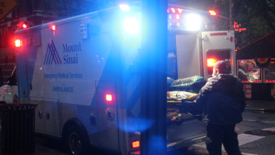 Photograph of an EMT worker placing a stretcher back into an ambulance for Mount Sinai on the street. 
