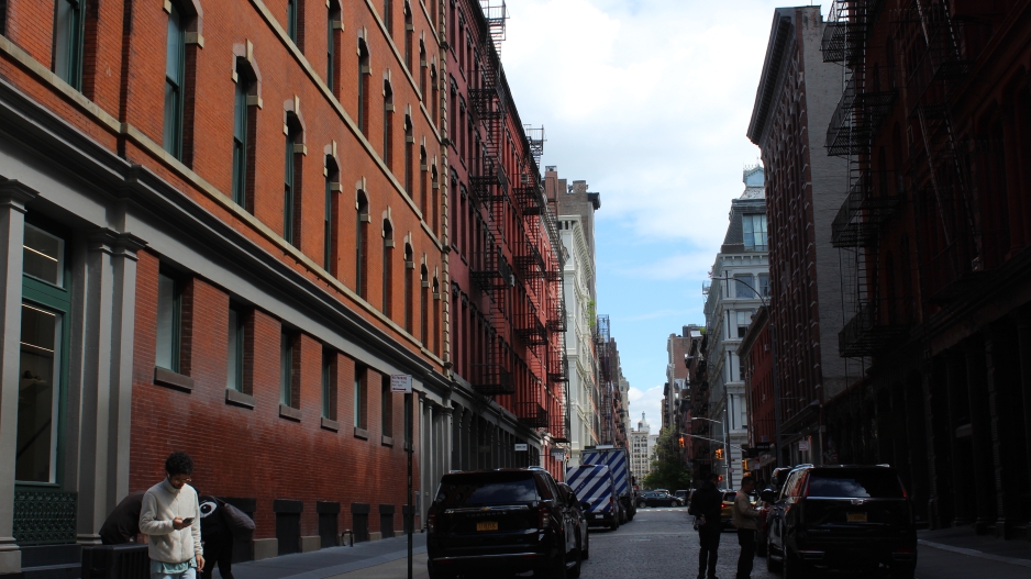 Photograph of buildings in soho with red brick from the middle of the cobblestone street. Young man looking at his phone in the bottom left of picture