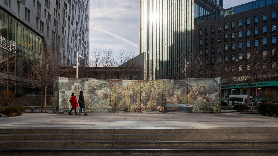 An art installation of large pictures on a wall is shown between high rises on a city street. 