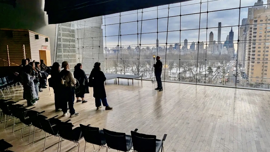 Students looking at the speaker in front of huge windows in Lincoln Center Apple Room.