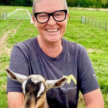 Non-binary person in a country setting holding a baby goat