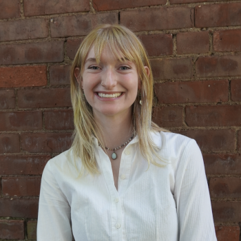 Smiling woman stands in front of brick wall.