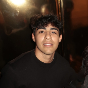 Man with tan skin and dark hair wearing black sweater and smiling