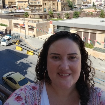 A white woman with curly brown hair standing in front of a hillside city
