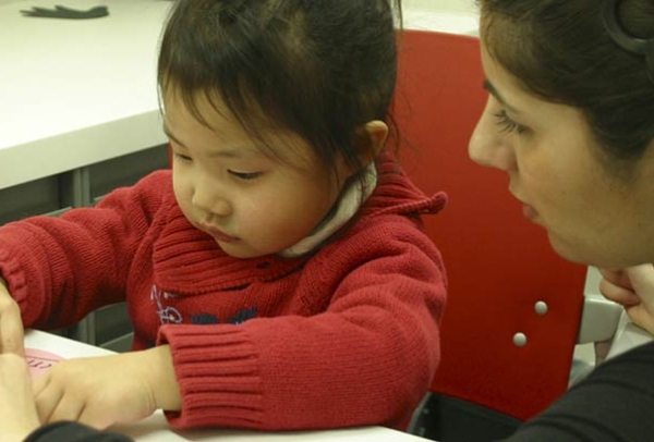 A speech-language pathologist working on an activity with a small child in red.