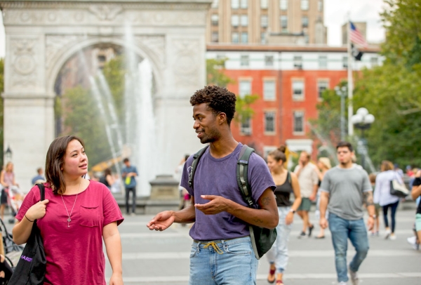 Two graduate students walking through Washington Square Park with the fountain and arch in the background